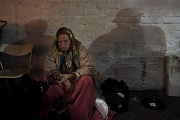 Una mujer sin hogar come una pieza de fruta en la calle, mientras que el reflejo de la pared muestra la figura de otros dos vagabundos. (AP/Jae C. Hong).