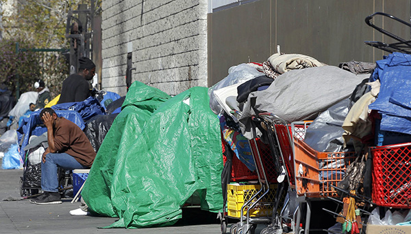 Una persona sin hogar, sentada en la calle entre sus posesiones en Los Ángeles (AP)